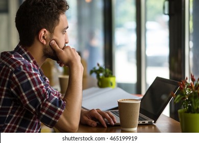 Handsome Man Working In Restaurant Or Cafe. Man Sitting In Front Of Laptop Computer And Thinking About Business Projects.