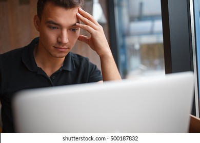 Handsome Man Working In Restaurant Or Cafe. Closeup Man Face Sitting In Front Of Laptop Computer And Thinking About Business Projects.