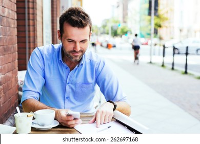 Handsome Man Working With Smartphone And Documents At Outdoor Cafe