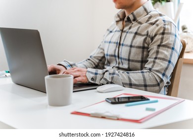 Handsome man working using computer laptop and drinking a mug of coffee with thinking serious face in modern bright office