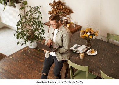 Handsome manager, man in glasses sits on table, holds laptop and types, sends message, works on project, drinks coffee, spends time at co-working space or an office. - Powered by Shutterstock