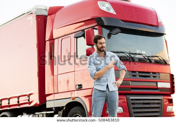 handsome masculine truck driver\
standing outside with his vehicle behind with pointing his\
car