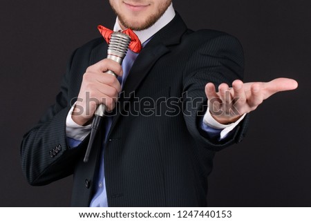 Handsome Master of ceremonies in black suit holding microphone in hand on black background. Showman, tv. closeup