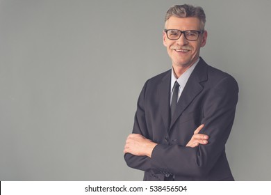 Handsome mature businessman in formal clothes and eyeglasses is looking at camera and smiling, on gray background - Shutterstock ID 538456504