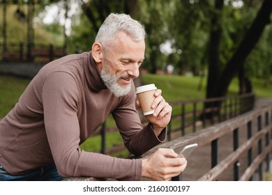 Handsome mature caucasian man using smartphone, calling his friends, colleagues, wife with good connection, texting online, surfing social media drinking coffee outdoors in park forest. - Powered by Shutterstock