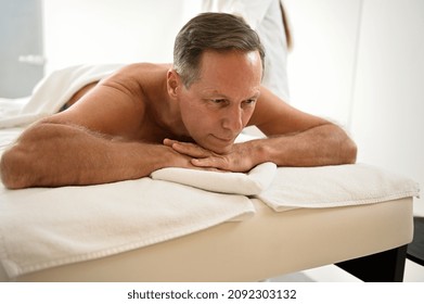 Handsome Mature European 50 Years Old Man Lying On A Massage Table At Wellness Spa Clinic. Alternative Physical Therapy And Professional Body Care Concept