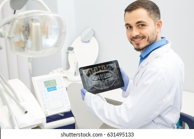 Handsome mature male dentist smiling to the camera over his shoulder holding a digital tablet displaying dental x-ray copyspace technology using doctor experience modern dentistry health medical - Powered by Shutterstock