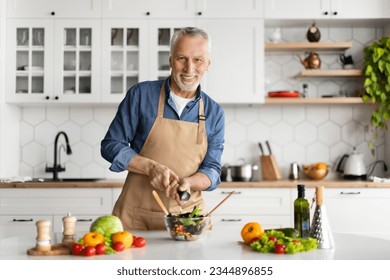 Handsome Mature Man Adding Salt To Salad While Cooking At Home, Happy Elderly Gentleman In Apron Posing In Kitchen Interior While Preparing Tasty Healthy Meal, Smiling At Camera, Copy Space - Powered by Shutterstock