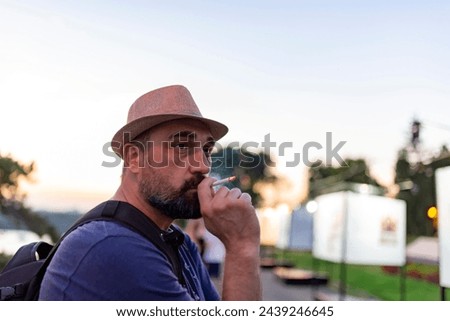Handsome Mature Man with Beard and Hat Smoking a Cigarette During a Sunset in the City