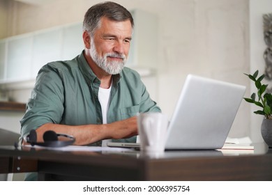 Handsome mature man in casual suit sitting at the table in home office and working at laptop - Powered by Shutterstock