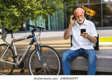 Handsome mature man listening his favorite music on a park bench. Senior man listening his favorite song with bike nearby. - Powered by Shutterstock