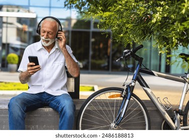 Handsome mature man listening his favorite music on a park bench. Senior man listening his favorite song with bike nearby. - Powered by Shutterstock