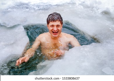Handsome mature man smiles and bathes in a winter ice hole.