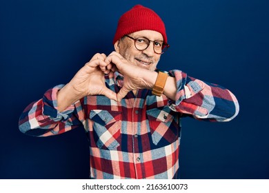 Handsome mature man wearing hipster look with wool cap smiling in love doing heart symbol shape with hands. romantic concept. 