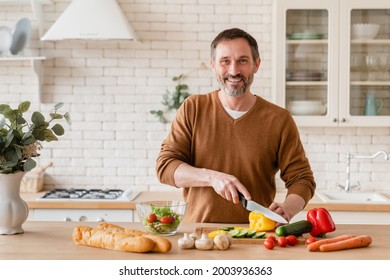 Handsome mature middle-aged man husband father cooking vegetable salad in the kitchen at home, preparing vegetarian food meal cutting bell pepper on cutting board. Homemade meal