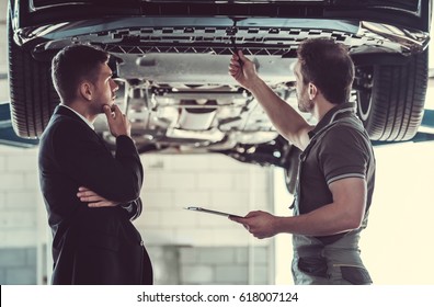 Handsome Mechanic And Businessman Are Examining Car And Discussing Repair In Auto Service