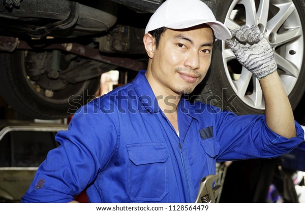 Handsome Mechanic holding wrench on hand to inspection.\
maintenance and people concept. Man with equipment at car repair\
service or auto store. mechanic holding out a wrench raised car\
background 