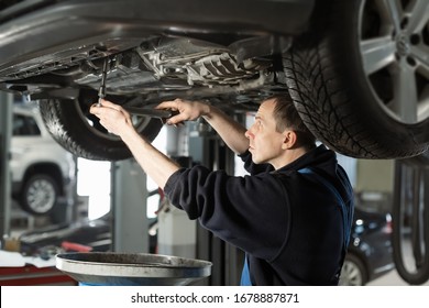 Handsome mechanic in uniform is working in auto service with lifted vehicle. Car repair and maintenance. Oil change