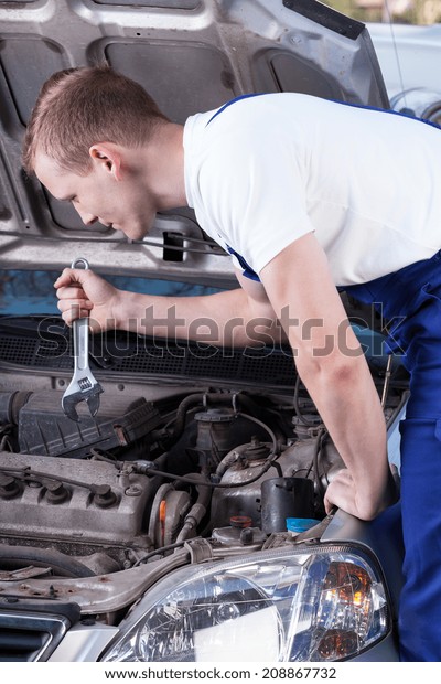 Handsome mechanic\
with wrench fixing car\
engine