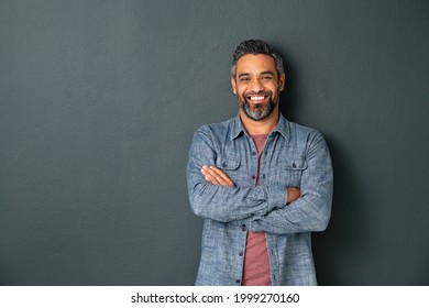 Handsome mid adult man with beard and crossed arms looking at camera. Mature middle eastern man isolated against grey wall and smiling. Satisfied indian guy looking at camera with a big laugh.
