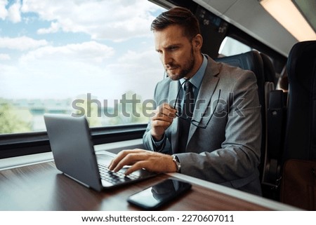 Handsome middle age businessman using his laptop computer while traveling with high-speed train. Modern and fast travel concept.
