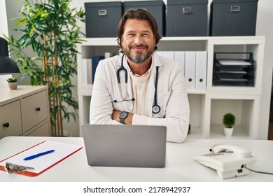 Handsome middle age doctor man working at the clinic happy face smiling with crossed arms looking at the camera. positive person.  - Powered by Shutterstock