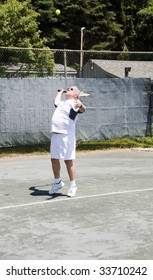 Handsome Middle Age Male Tennis Player Serving With Ball In Air On Tennis Court At Club