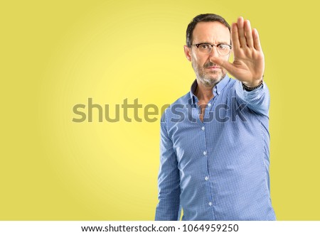 Handsome middle age man annoyed with bad attitude making stop sign with hand, saying no, expressing security, defense or restriction, maybe pushing