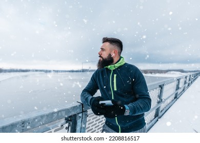 Handsome middle age man with a beard running and exercising outside on extremely cold and snowy day. Sport and fitness motivation theme. He using smart phone to track his activity data. - Shutterstock ID 2208816517