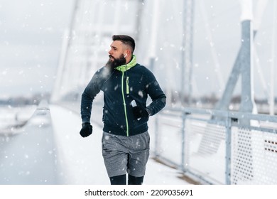 Handsome middle age man with a beard running and exercising outside on extremely cold and snowy day. Sport and fitness motivation theme. - Shutterstock ID 2209035691