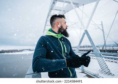 Handsome middle age man with a beard running and exercising outside on extremely cold and snowy day. Sport and fitness motivation theme. He using smart phone to track his activity data. - Shutterstock ID 2214584491