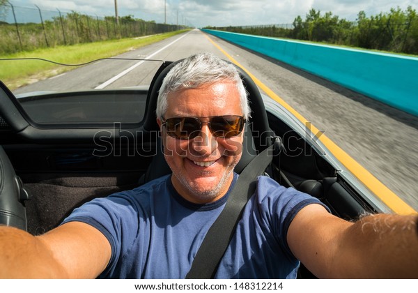 Handsome middle age man driving a convertible\
automobile on the\
highway.