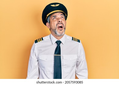 Handsome Middle Age Man With Grey Hair Wearing Airplane Pilot Uniform Angry And Mad Screaming Frustrated And Furious, Shouting With Anger. Rage And Aggressive Concept. 