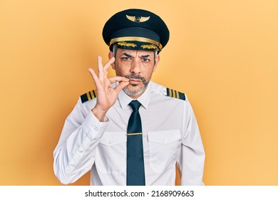 Handsome middle age man with grey hair wearing airplane pilot uniform mouth and lips shut as zip with fingers. secret and silent, taboo talking 