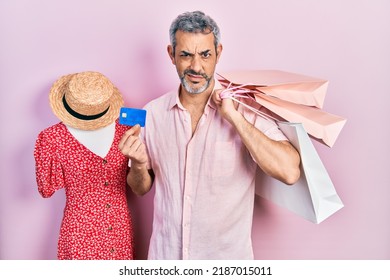 Handsome Middle Age Man With Grey Hair Holding Shopping Bags And Credit Card Clueless And Confused Expression. Doubt Concept. 