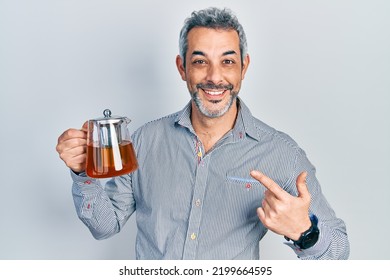 Handsome Middle Age Man With Grey Hair Holding Traditional Tea Pot Smiling Happy Pointing With Hand And Finger 