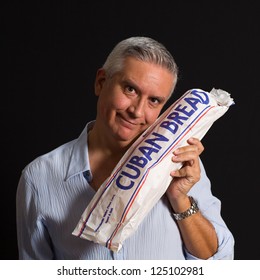 Handsome Middle Age Man  Holding A Loaf Of Cuban Bread On A Black Background.