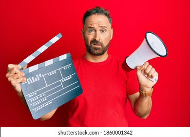 Handsome Middle Age Man Holding Video Film Clapboard And Megaphone Clueless And Confused Expression. Doubt Concept. 