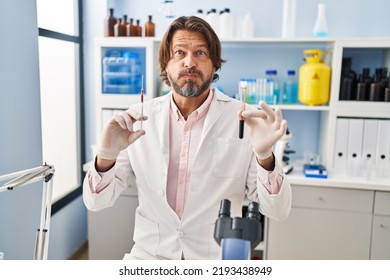 Handsome Middle Age Man Holding Blood Sample At Biology Laboratory Puffing Cheeks With Funny Face. Mouth Inflated With Air, Catching Air. 