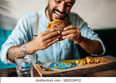 Handsome middle age man sitting in restaurant and enjoying in delicious burger. 