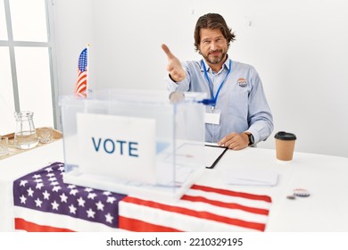 Handsome Middle Age Man Sitting At Voting Stand Smiling Friendly Offering Handshake As Greeting And Welcoming. Successful Business. 