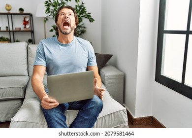 Handsome middle age man using computer laptop on the sofa angry and mad screaming frustrated and furious, shouting with anger. rage and aggressive concept.  - Shutterstock ID 2079581464