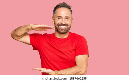 Handsome Middle Age Man Wearing Casual Red Tshirt Gesturing With Hands Showing Big And Large Size Sign, Measure Symbol. Smiling Looking At The Camera. Measuring Concept. 