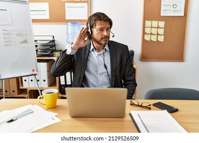 Handsome Middle Age Man Wearing Call Center Agent Headset At The Office Smiling With Hand Over Ear Listening An Hearing To Rumor Or Gossip. Deafness Concept. 