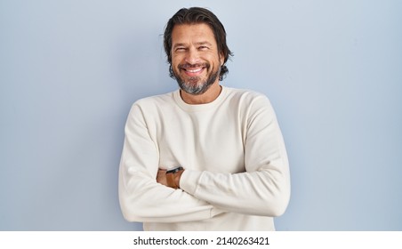 Hombres guapos de mediana edad con suéter casual sobre fondo azul cara feliz sonriendo con los brazos cruzados mirando la cámara. persona positiva. 