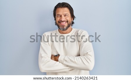 Handsome middle age man wearing casual sweater over blue background happy face smiling with crossed arms looking at the camera. positive person. 