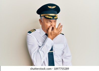 Handsome Middle Age Mature Man Wearing Airplane Pilot Uniform Smelling Something Stinky And Disgusting, Intolerable Smell, Holding Breath With Fingers On Nose. Bad Smell 