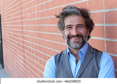 Handsome Middle Age Mediterranean Man In A Studio Portrait On A Red Brick Wall Background Smiling With Copy Space