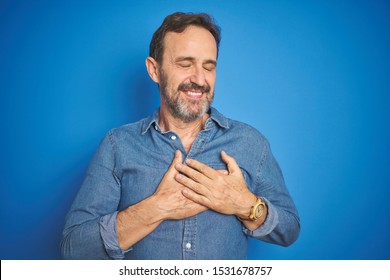 Handsome Middle Age Senior Man With Grey Hair Over Isolated Blue Background Smiling With Hands On Chest With Closed Eyes And Grateful Gesture On Face. Health Concept.