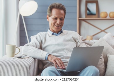 Handsome middle aged businessman is using a laptop and smiling while working at home